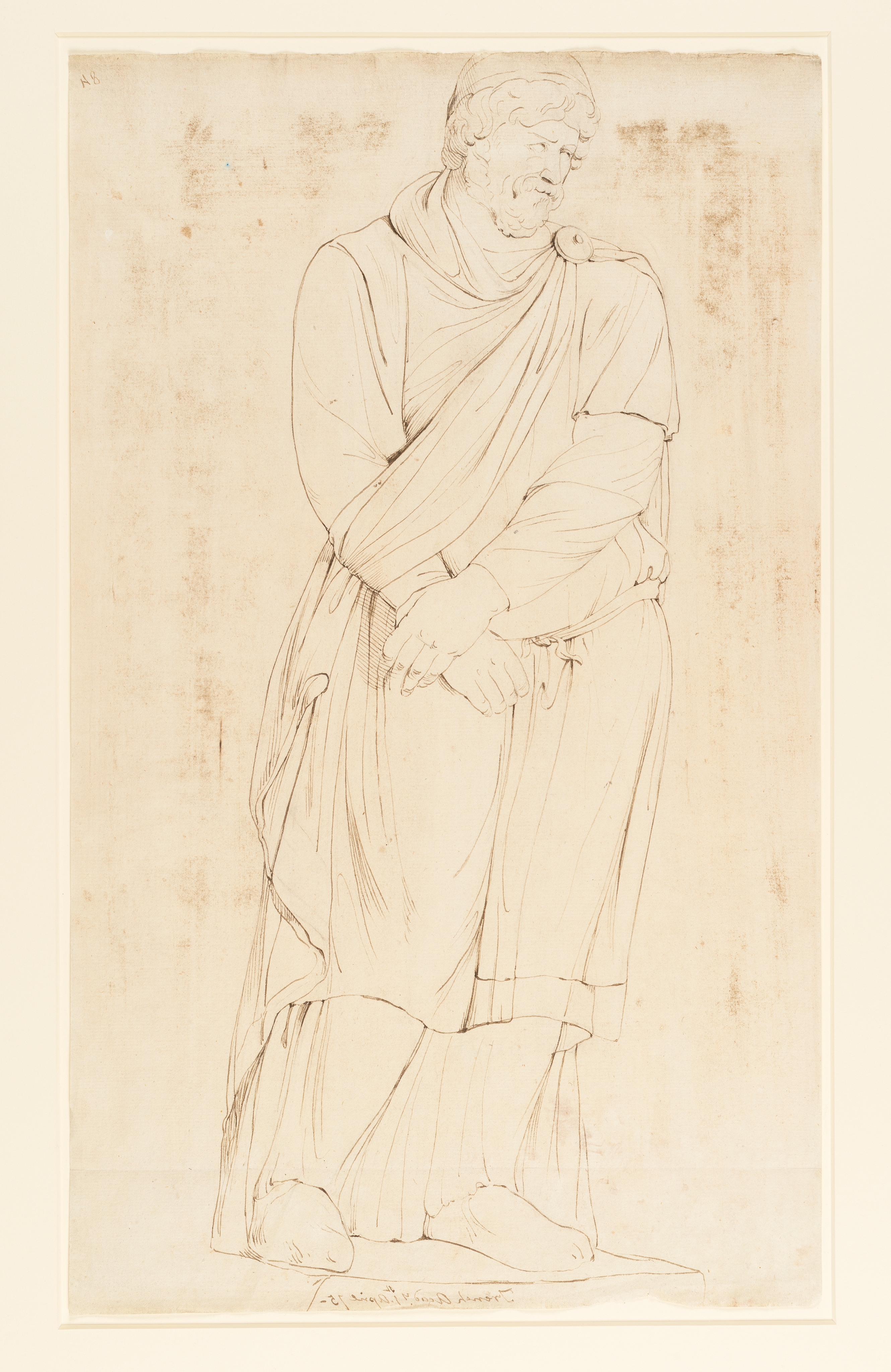 Drawing of a male figure, standing, with his hands clasped. It is a study of an unidentified ancient sculpture or cast. The figure wears a beard and moustache. His dress consists of layered garments tied at the waist. His right hand clasps his left before him. Around his left arm is a sash, which runs from a round broach at his right shoulder, and down around his arm in  the manner of a sling. Inscribed on recto, along pedestal edge (handwritten in ink): 'French Acady. 1st April 75-'  and to upper right (handwritten in ink): '84'. An historic fold line runs across the drawing 65 mm up from the bottom edge of the sheet. Made by Joseph Wright of Derby (1734 - 1797), 1775. Pen and ink and brown wash, over pencil on laid paper. Displayed in a cream window mount.