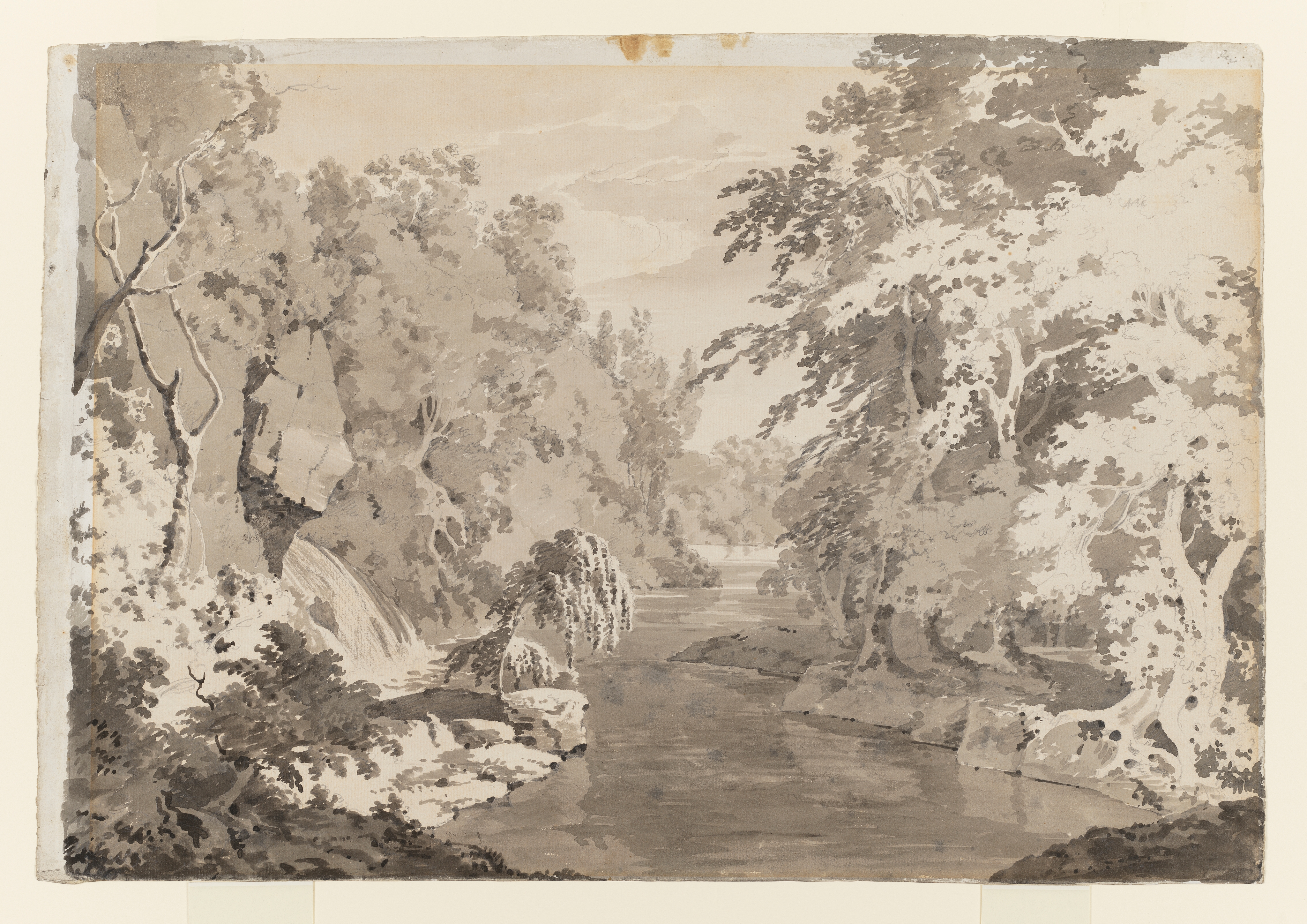 Study of a landscape with a river, identified as a view in Dovedale, Derbyshire. Inscribed on verso (handwritten in ink): 'T G 1798'. Made by Joseph Wright of Derby (1734 - 1797), c.1786. Ink wash over pencil on laid paper. Displayed in a cream window mount.