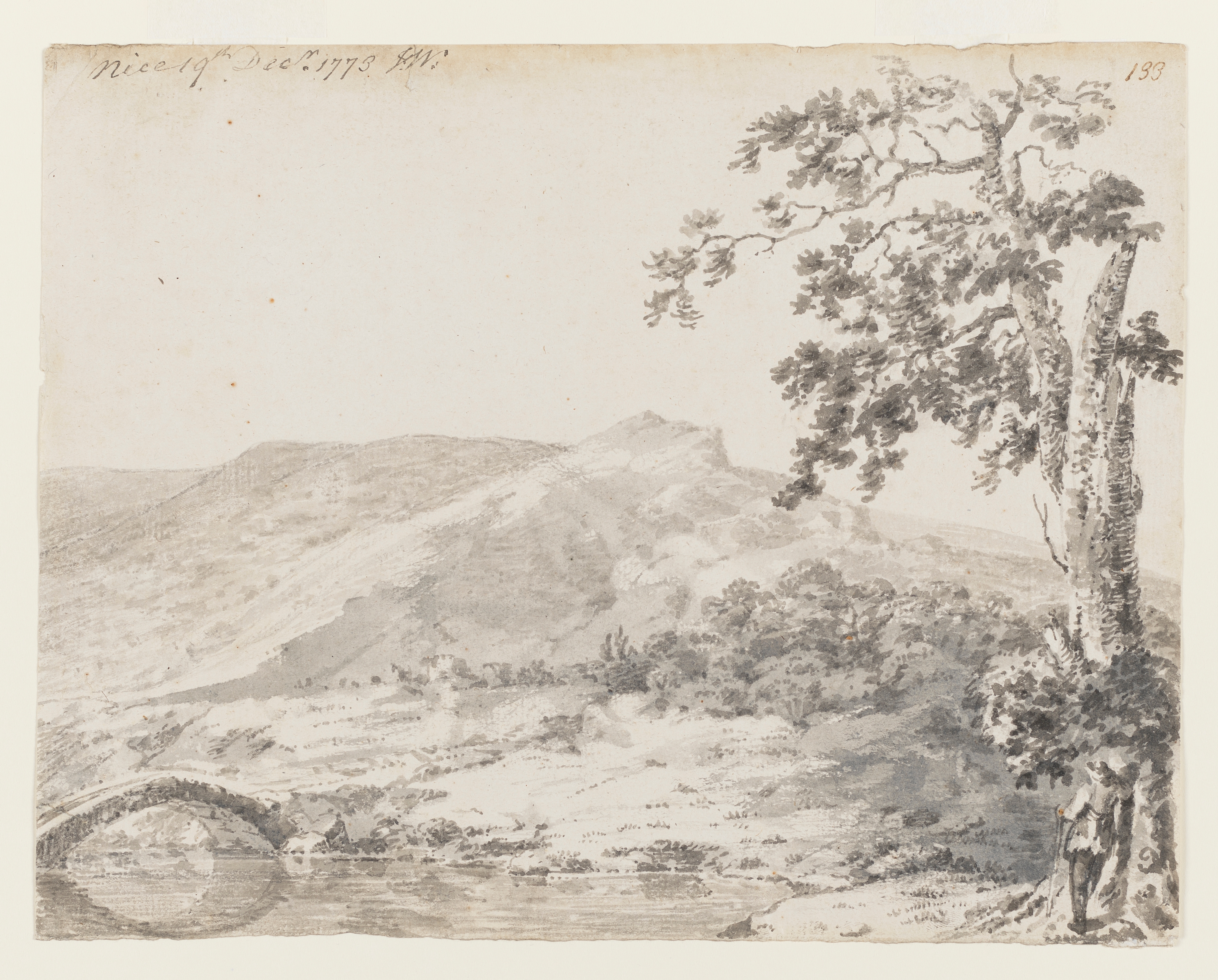 Drawing of a landscape, identified as a view in or near Nice. In the foreground, a river runs beneath a simple arched bridge. To the right is a tree, against which a figure leans, with his back to us, looking at the hilly terrain beyond. Inscribed along top left edge of sheet (handwritten in ink): 'Nice 19th Decr. 1773 J.W.' and to top right corner: '133'. Made by Joseph Wright of Derby (1734-1797), 1773. Grey ink wash on paper. Displayed in cream window mount.