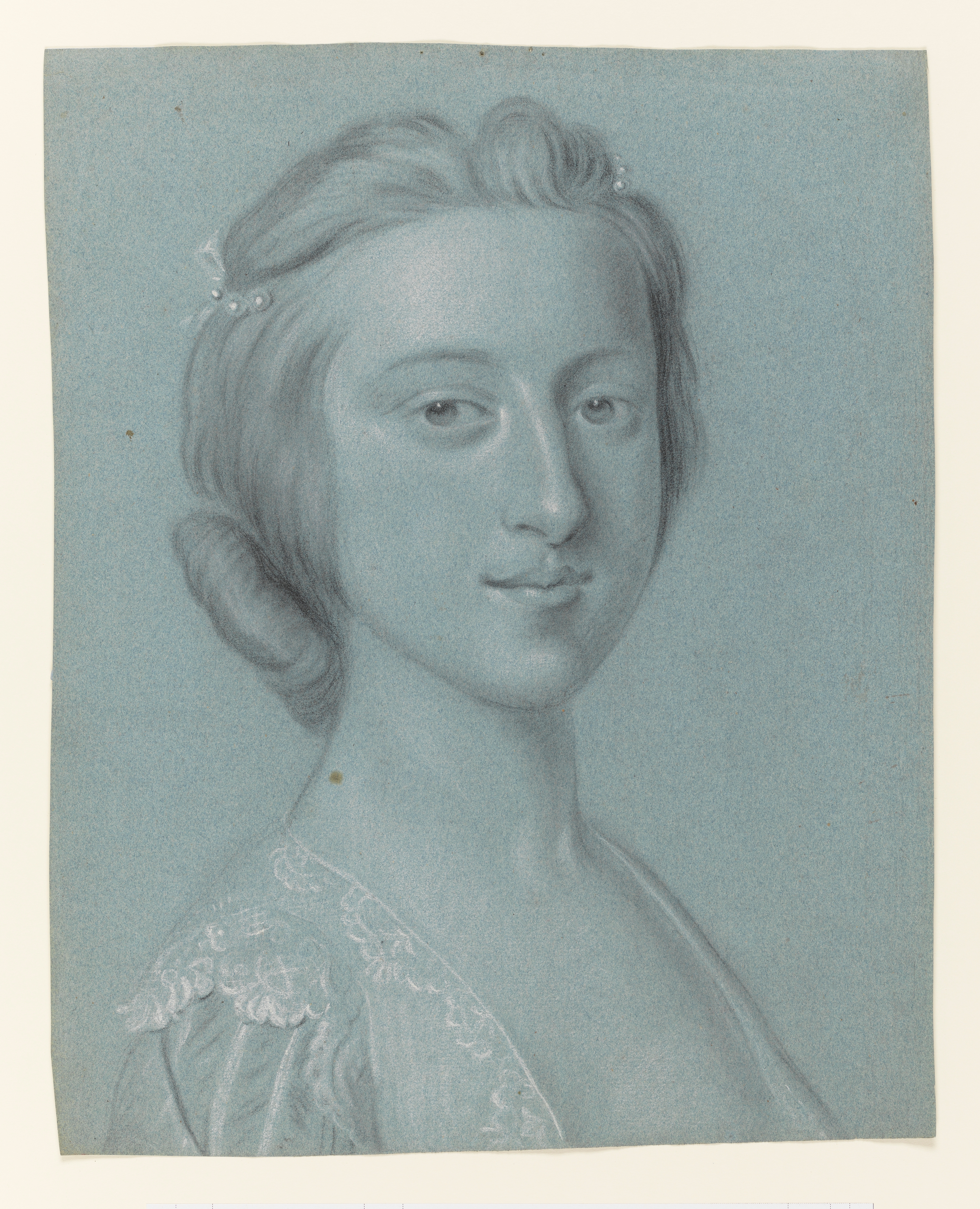 Study of a young woman, head and shoulders only, facing right; wearing a lace edged gown, her hair dressed with ribbons and pearls. Made by Joseph Wright of Derby (1734 - 1797). Black and white chalk on blue paper, in cream window mount.